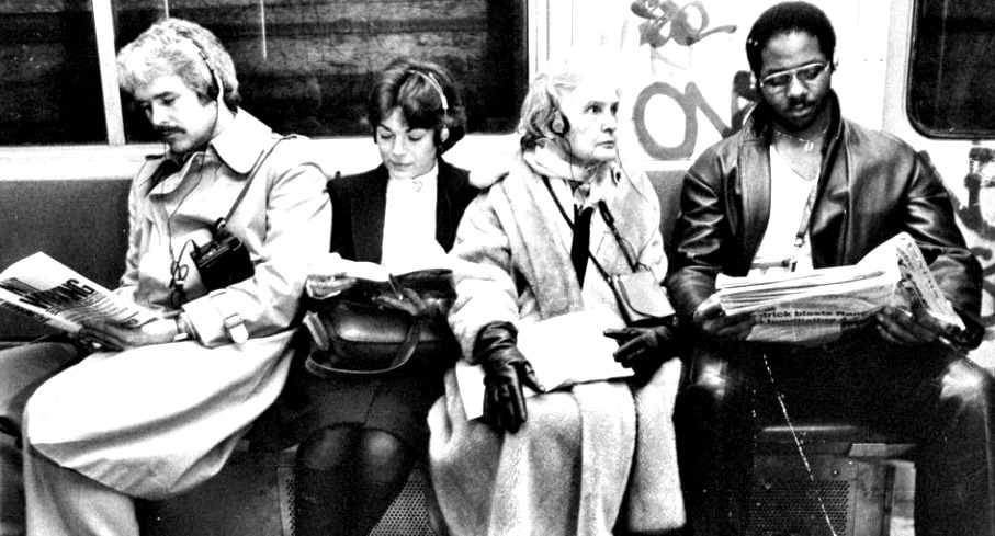 Four passegers in a subway train listening to thier mobile personal music playing devices with little on-ear headphones